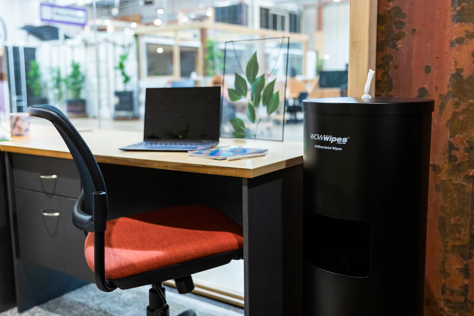 a black wipes dispenser next to an office desk.